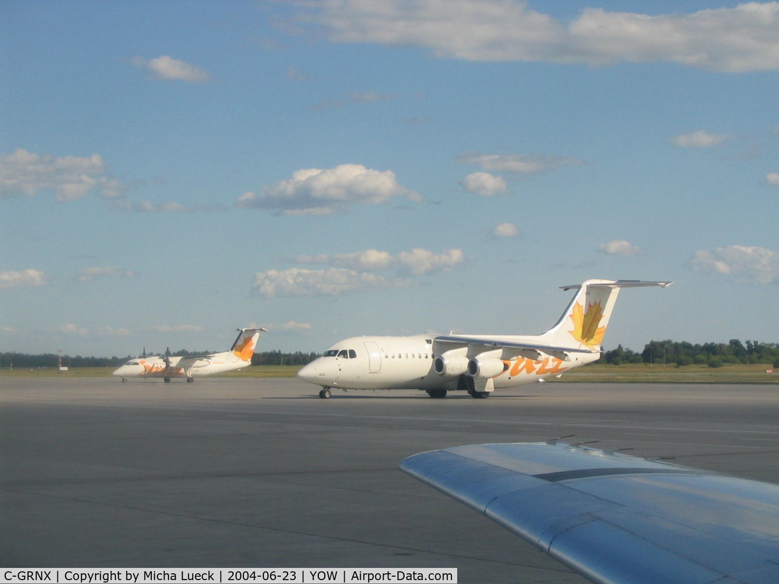 C-GRNX, 1989 British Aerospace BAe.146-200 C/N E2130, BAe 146 and Dash 8, both in the yellow Air Canada Jazz colour scheme, see over the wing of JetsGo's F100 C-GKZA