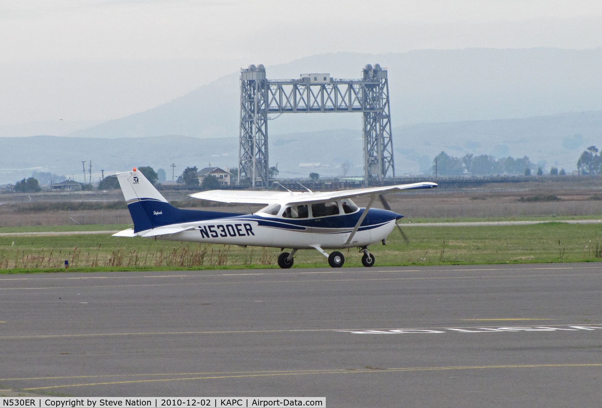 N530ER, 2002 Cessna 172S C/N 172S9113, Bacchus Aviation (Sonoma Skypark, CA) 2002 Cessna 172S taxis with Napa River RR Bridge in background @ Napa County Airport, CA