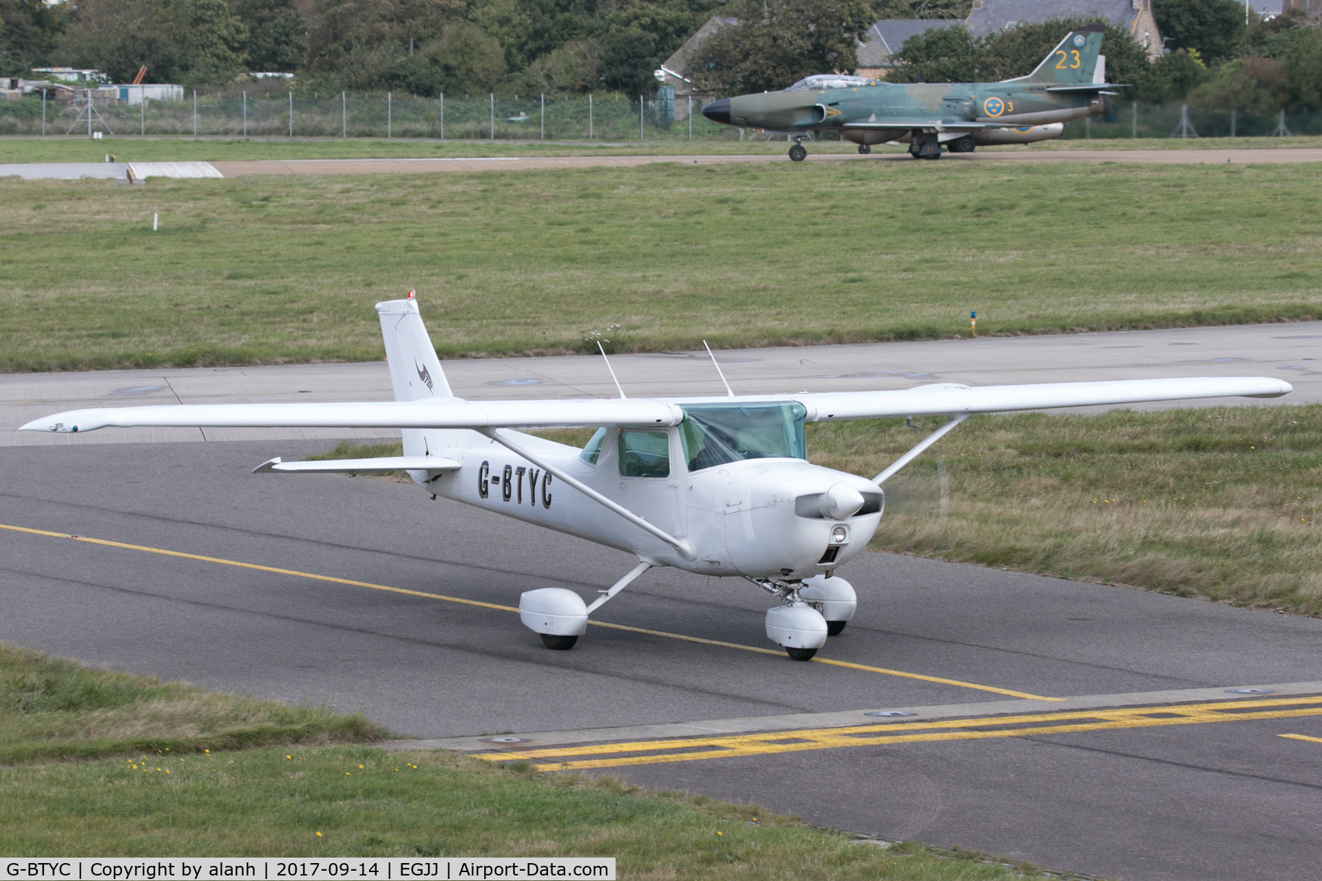 G-BTYC, 1975 Cessna 150L C/N 150-75767, Taxiing to the aero club at Jersey; the Swedish Historic Flight Lansen & Tunan are about to launch for a display rehearsal in the background.