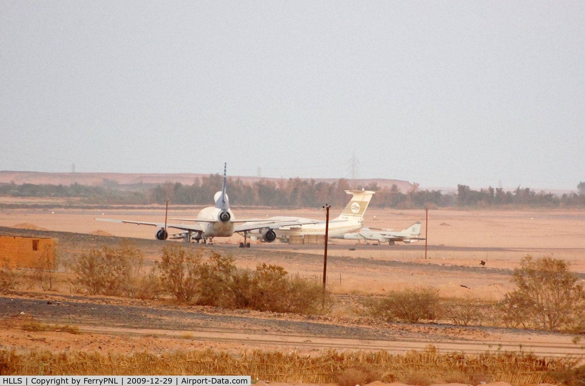Sebha Airport, Sebha Libyan Arab Jamahiriya (HLLS) - Remote stand with stored L1011 of Kallat El-Saker Air Company (one of three), a Il76 of LAA and a MIG29. View from hotel.