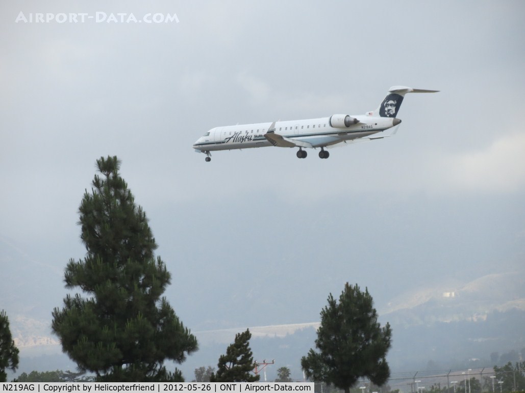 N219AG, 2006 Bombardier CRJ-701 (CL-600-2C10) Regional Jet C/N 10246, Passing over the trees and the outer fence for 26R